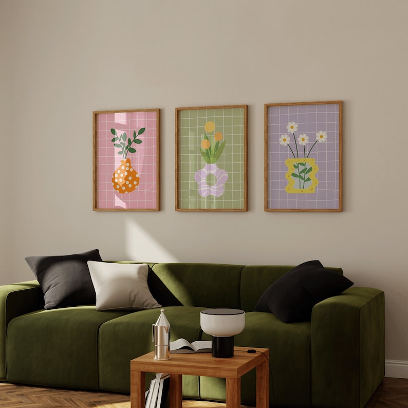 May include: Three framed art prints with floral illustrations. Each print has a wooden frame and a grid background. The artwork includes vases with flowers and foliage in orange, yellow, and white, set against pink, green, and purple backgrounds.