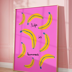 Może przedstawiać: R&oacute;żowy wydruk w ramie z tekstem "life is bananas" napisanym czarnym, ozdobnym pismem. Tło jest r&oacute;żowe z ż&oacute;łtymi bananami z niebieskimi konturami.