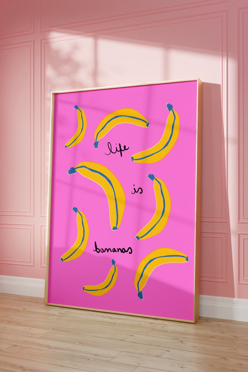 Może przedstawiać: R&oacute;żowy wydruk w ramie z tekstem "life is bananas" napisanym czarnym, ozdobnym pismem. Tło jest r&oacute;żowe z ż&oacute;łtymi bananami z niebieskimi konturami.