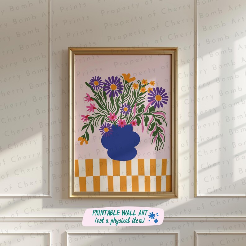 以下が含まれることがあります： 青い花瓶に活けられた鮮やかな花の絵が額装されています。花は紫、オレンジ、ピンクで、薄いピンク色の背景に配置されています。花瓶は、黄色と白の市松模様のテーブルの上に置かれています。下部のテキストは「PRINTABLE WALL ART（not a physical item）」です。