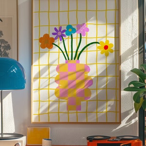 May include: A framed wall art print featuring a checkered pink and yellow vase holding five colorful flowers in orange, purple, blue, pink, and yellow. The background consists of a white surface with a yellow grid pattern of thin vertical and horizontal lines.