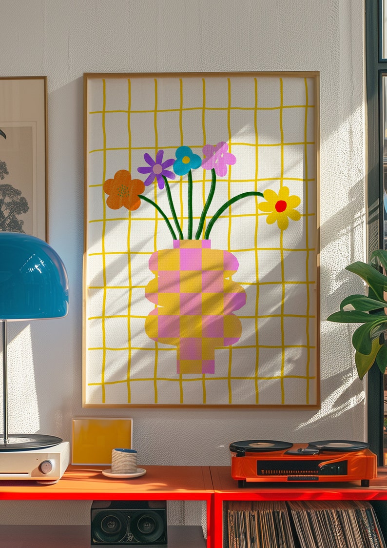 May include: A framed wall art print featuring a checkered pink and yellow vase holding five colorful flowers in orange, purple, blue, pink, and yellow. The background consists of a white surface with a yellow grid pattern of thin vertical and horizontal lines.