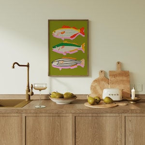 Puede incluir: Una impresi&oacute;n art&iacute;stica enmarcada con tres ilustraciones de peces coloridos sobre un fondo verde. Los peces tienen detalles en rojo, verde y naranja. La escena de la cocina incluye un grifo, una copa, un cuenco de peras, tablas de cortar y una tostadora.