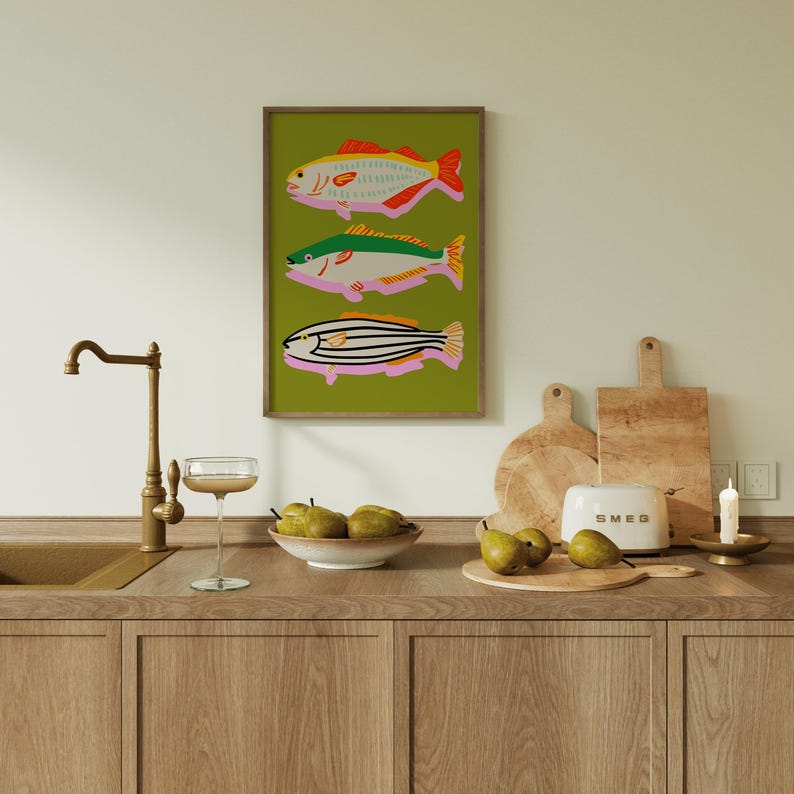Puede incluir: Una impresi&oacute;n art&iacute;stica enmarcada con tres ilustraciones de peces coloridos sobre un fondo verde. Los peces tienen detalles en rojo, verde y naranja. La escena de la cocina incluye un grifo, una copa, un cuenco de peras, tablas de cortar y una tostadora.