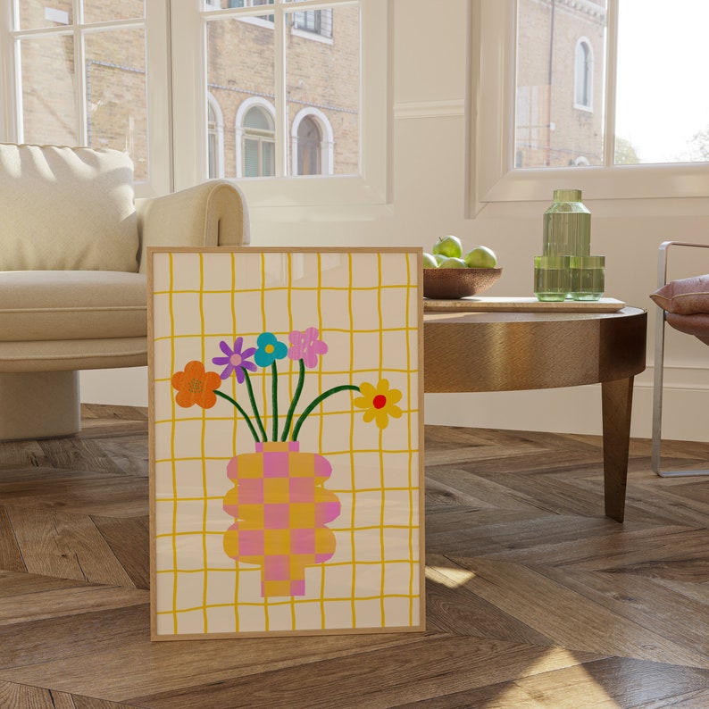 May include: A framed wall art print featuring a checkered pink and yellow vase holding five colorful flowers against a yellow grid background. The flowers are orange, purple, blue, pink, and yellow with a red center, all rendered in a flat graphic style.