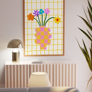 May include: A rectangular framed wall art print featuring a white background with a yellow grid pattern. The central illustration depicts a pink and orange checkered vase holding a bouquet of colorful flowers in orange, purple, blue, and yellow.
