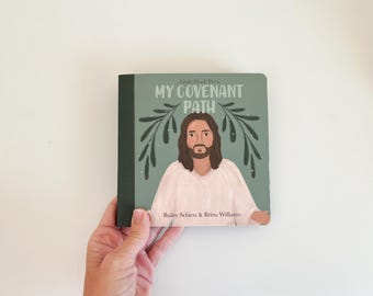 May include: A book titled "My Covenant Path" with a green cover featuring an illustration of a man with long brown hair and a beard. The book has a dark green spine and is held by a hand.
