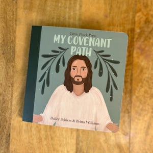 May include: A children's book titled "My Covenant Path" with an illustration of a figure in white robes and long brown hair. The cover is light blue with text and olive branch designs. Authors are Bailey Schiess & Britta Williams.