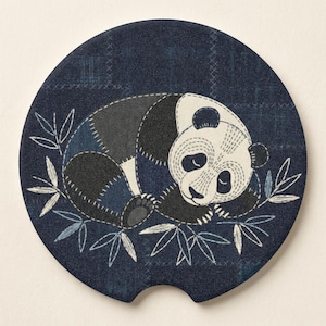 May include: A round car coaster featuring a sleeping panda bear design. The panda is depicted in black, white, and gray patchwork, resting on a bed of bamboo leaves. The background is a dark blue fabric with stitched details.