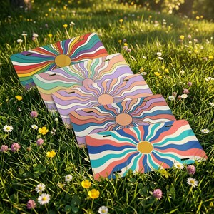 May include: Four license plates with a retro sunburst design in various colors, including red, orange, yellow, green, blue, and purple. Each plate features a central yellow sun and radiating lines. The plates are displayed on a bed of green grass.