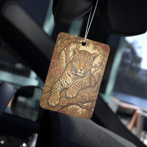 May include: Rectangular car air freshener featuring a detailed illustration of a leopard resting on a tree branch. The design incorporates floral and tree elements in shades of brown, beige, and orange. The air freshener is suspended by a white string.