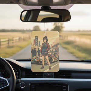 May include: Rectangular car air freshener featuring an anime-style illustration of a woman in a racing jacket and skirt, standing in front of a race car. The air freshener is hanging from a car's rearview mirror.