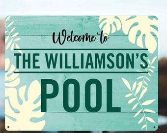 May include: A rectangular sign with the words "Welcome to THE WILLIAMSON'S POOL" in black and green. The sign has a teal background with cream-coloured leaf accents and is mounted on a wooden post.