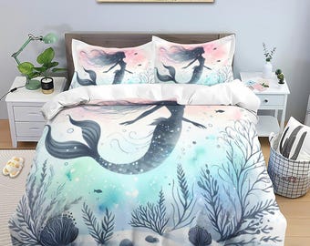 Könnte beinhalten: Ein weiß-blaues Meerjungfrauen-Bettwäsche-Set mit einem Aquarell-Design einer Meerjungfrau, die in einem Meer aus Blasen und Seegras schwimmt. Die Meerjungfrau ist eine Silhouette mit einem rosa-blauen Ombre-Effekt.