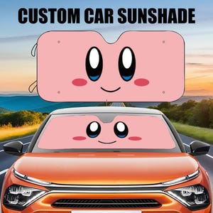 May include: A pink car sunshade with a cartoon face. The sunshade has two large eyes, a smiling mouth, and rosy cheeks. The sunshade is installed in the front windshield of a car.