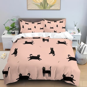 May include: A pink duvet cover with a black cat pattern. The duvet cover has a repeating pattern of black cats with yellow eyes on a light pink background.