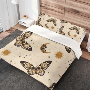 May include: A cream-colored bedding set with a celestial and butterfly pattern. The pattern features black butterflies, moons, stars, and suns in gold and brown.