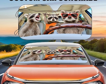 May include: Custom car sunshade featuring a colorful image of four raccoons wearing sunglasses and driving a car. The sunshade is designed to fit most car windshields.