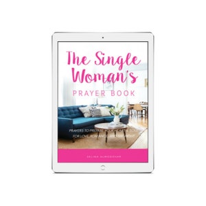 May include: A white tablet computer displaying a pink and white book cover with the title "The Single Woman's Prayer Book". The cover features a photo of a living room with a blue sofa, a coffee table, and a vase of white flowers.