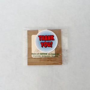 May include: A small package with a round sticker that says "THANK YOU!" in red text with a blue background. The package is wrapped in clear plastic and includes text that reads "Made with NATIVIA bio-based film".