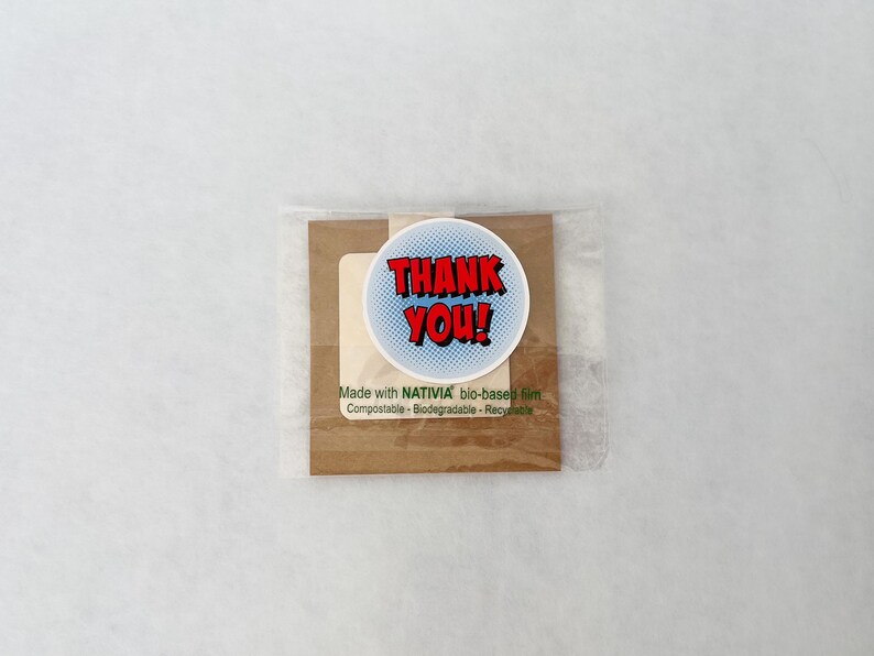 May include: A small package with a round sticker that says "THANK YOU!" in red text with a blue background. The package is wrapped in clear plastic and includes text that reads "Made with NATIVIA bio-based film".