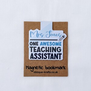 May include: A magnetic bookmark with the text "Mrs Jones ONE AWESOME TEACHING ASSISTANT" in blue and black. The bookmark has a pencil graphic and is on a brown card with the text "Magnetic bookmark" and a website address.