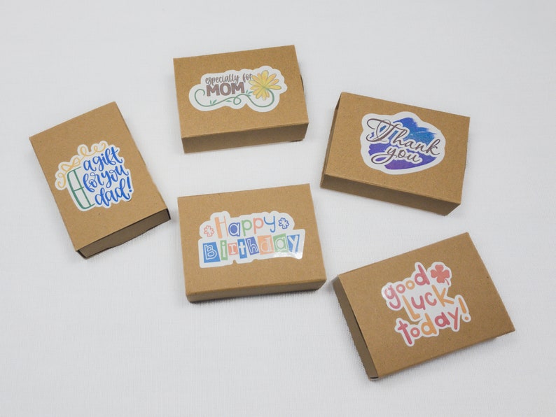May include: Five small, brown cardboard gift boxes with colourful stickers. The stickers read: "A gift for you dad!", "Especially for MOM", "Happy Birthday", "Thank you", and "Good luck today!"