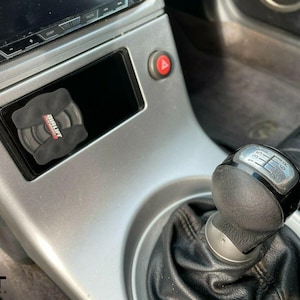 May include: A close-up of a silver car's interior with a black leather gear shift knob. The gear shift knob has a silver ring around it and the numbers 1, 3, 5, R printed on it. The car's interior is silver and has a black leather seat.