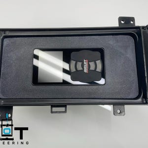 May include: A black plastic box with a rectangular cutout for a screen and a smaller cutout for a black Air Lift controller. The box has a textured surface and a black trim around the edges.