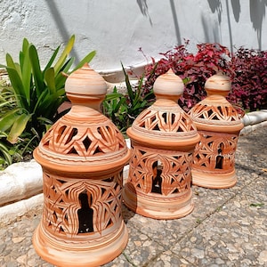 Peut inclure: Trois lanternes en terre cuite avec des motifs sculpt&eacute;s complexes. Les lanternes sont de couleur brun clair et ont un sommet en forme de d&ocirc;me. Elles sont dispos&eacute;es en rang&eacute;e sur une surface en pierre.