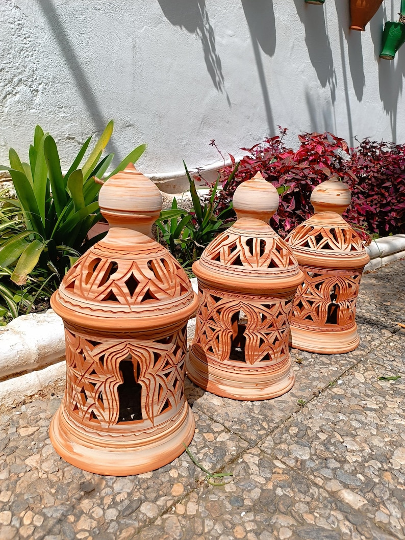 Peut inclure: Trois lanternes en terre cuite avec des motifs sculpt&eacute;s complexes. Les lanternes sont de couleur brun clair et ont un sommet en forme de d&ocirc;me. Elles sont dispos&eacute;es en rang&eacute;e sur une surface en pierre.