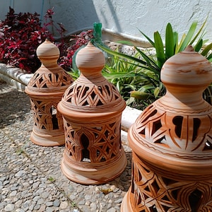 Peut inclure: Trois lanternes en terre cuite avec des motifs sculpt&eacute;s complexes. Les lanternes sont brunes et blanches avec une finition rustique.