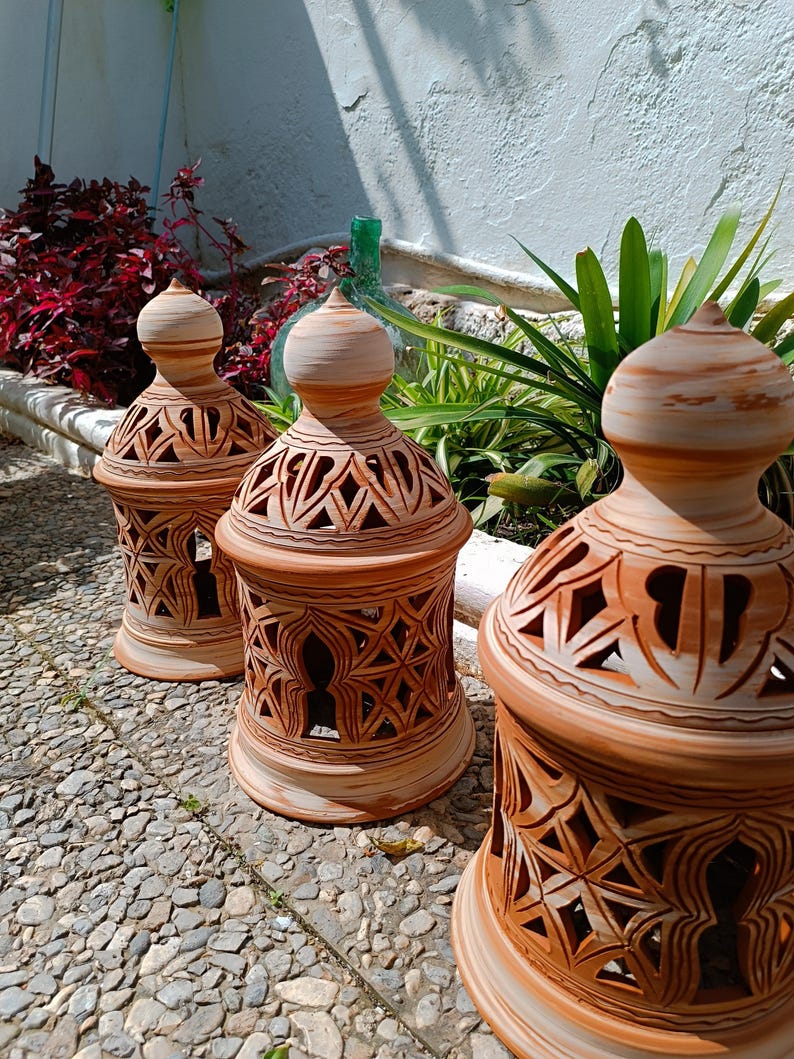 Peut inclure: Trois lanternes en terre cuite avec des motifs sculpt&eacute;s complexes. Les lanternes sont brunes et blanches avec une finition rustique.