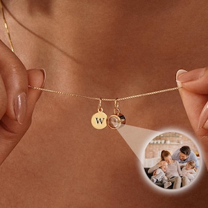 May include: A gold chain necklace with a small round charm engraved with the letter "W" and a larger round charm with a photo of a family inside.