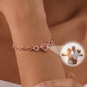 May include: A rose gold bracelet with a heart-shaped charm that reveals a photo when you open it. The charm is surrounded by smaller hearts with clear stones.