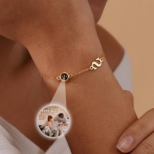 May include: A gold chain bracelet with a small round charm that reveals a photo of a family when viewed through a magnifying glass. The bracelet has a letter charm that says "M".