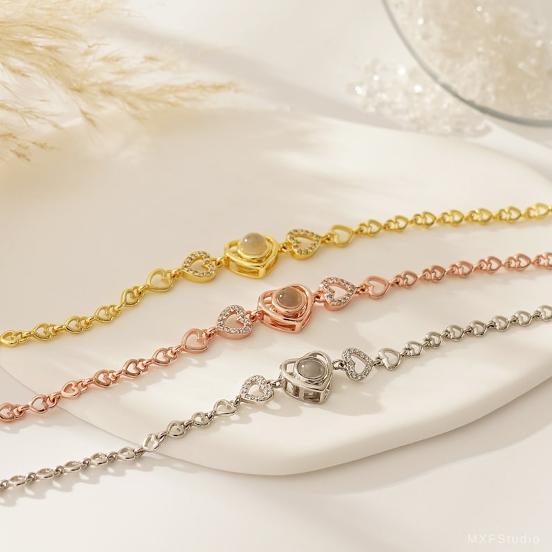Puede incluir: Tres pulseras en forma de coraz&oacute;n con una peque&ntilde;a piedra redonda y transparente en el centro de cada coraz&oacute;n. Las pulseras son de oro, oro rosa y plata.