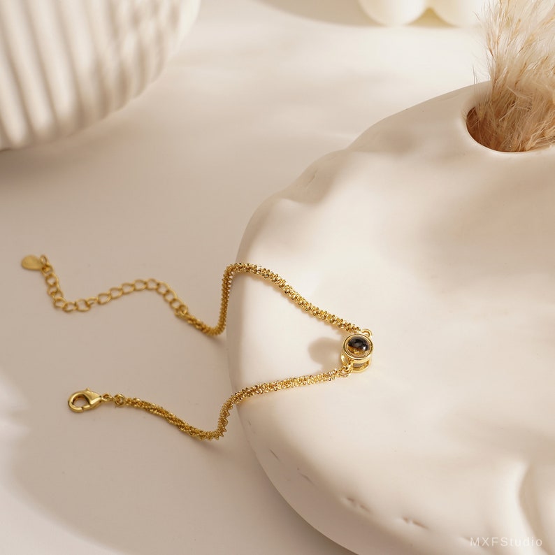 May include: A gold chain bracelet with a small round black stone pendant.