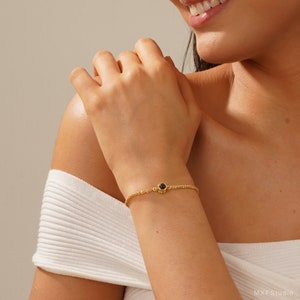May include: A gold chain bracelet with a small black gemstone charm.