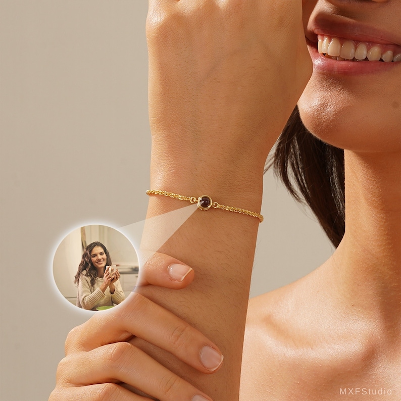 May include: A gold chain bracelet with a small, round, dark red gemstone. The bracelet is on a person's wrist.
