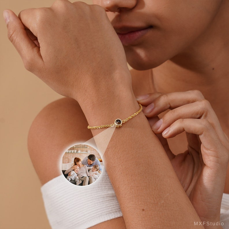 May include: A gold chain bracelet with a small round charm that reveals a photo when viewed through a magnifying glass. The charm is on a woman's wrist.