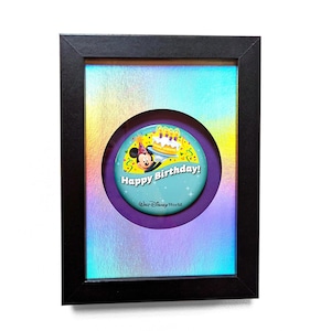 May include: A framed button featuring Mickey Mouse wearing a party hat and holding a birthday cake. The button is teal blue with white text that reads "Happy Birthday!" and "Walt Disney World." The frame is black with a holographic iridescent background.