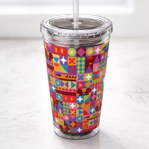 May include: A clear plastic tumbler with a lid and straw. The tumbler features a colorful geometric pattern in red, orange, yellow, blue, and green. The design includes shapes like squares, diamonds, and stars. The tumbler is designed for cold beverages.