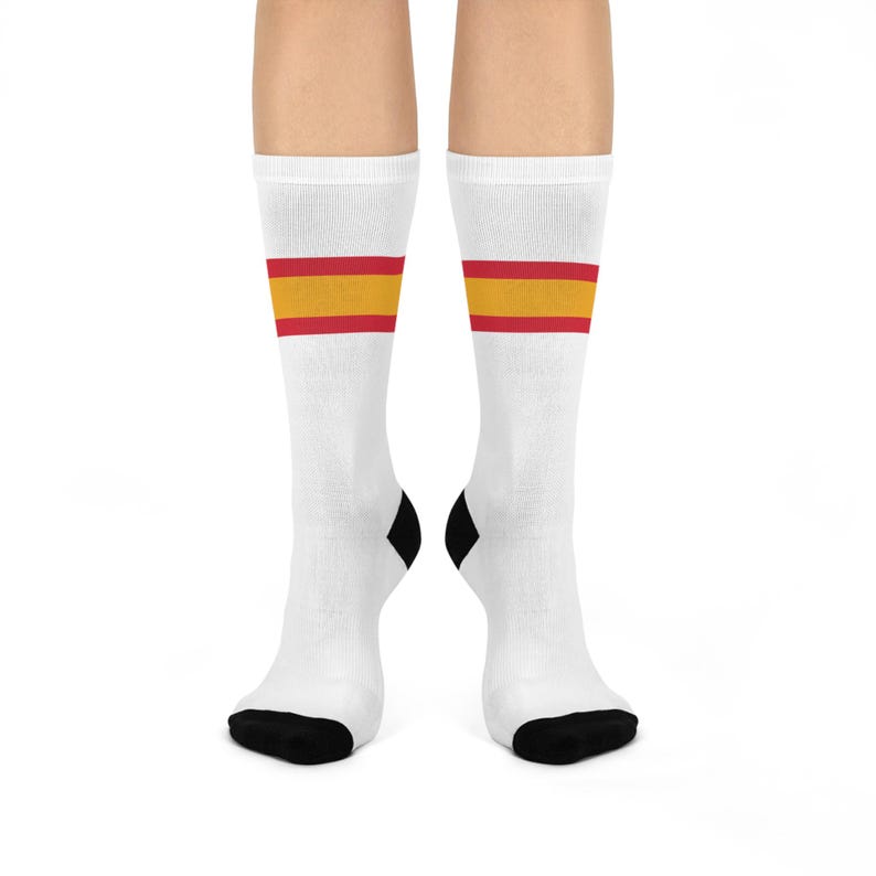 May include: White crew socks with a red and yellow stripe pattern. The socks have black heel and toe.