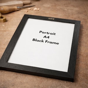 Pode incluir: Uma moldura preta com o texto "Portrait A4 Black Frame" em fundo branco. A moldura é retangular e tem um design simples e moderno. A moldura está sobre uma superfície de madeira.