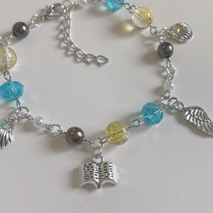 May include: A silver charm bracelet with blue, yellow, and white beads, a seashell charm, a book charm, and a wing charm.