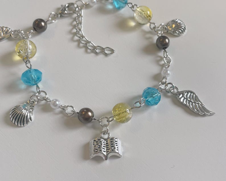 May include: A silver charm bracelet with blue, yellow, and white beads, a seashell charm, a book charm, and a wing charm.