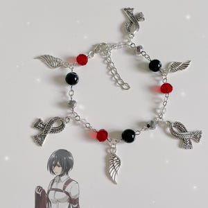 May include: Silver charm bracelet with red and black beads, featuring wings, ribbons, and other decorative charms.