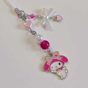 May include: A pink and white charm with a cartoon character wearing a pink hat and a pink bow. The charm is attached to a silver chain with pink and white beads and hearts.