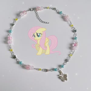 Op de afbeelding: Een zilveren ketting met roze, blauwe en gele kralen en vlinderbedels. De ketting heeft een bedel met een roze pony met een gele manen en staart.